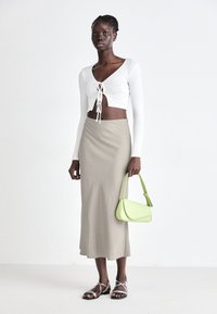 White ribbed crop top with lace-up front, beige maxi skirt, and light green handbag. Silver strappy sandals complete the look.