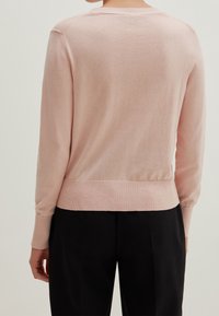 Jasnoróżowy dzianinowy sweter z okrągłym dekoltem, długimi rękawami i dopasowanym dołem. Gładka tekstura i delikatnie marszczone detale na rękawach.