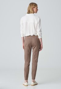 Weißes Blusenshirt mit umgeschlagenen Ärmeln, kombiniert mit braunen, taillierten Hosen aus einem weichen, strukturierten Stoff, ergänzt durch helle Sneakers.