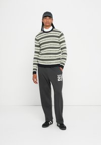 Gebreide trui met groene, zwarte en witte geometrische patronen; gecombineerd met grijze joggers met het witte "Hollister 22" logo; zwarte sneakers.