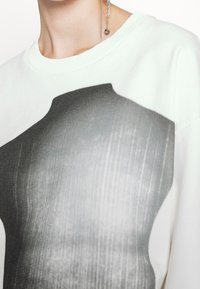 Vit sweatshirt med ett stort svart och grått grafiskt tryck av en bål, med en mjuk textur och ribbat nacke.
