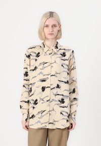 Beige button-down shirt featuring an abstract black and blue floral pattern, long sleeves, and a pointed collar. Smooth fabric texture.