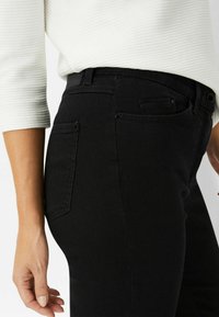 Jeans in denim nero con un design aderente, dotati di una tasca posteriore e dettagli di cucitura sottili. Texture liscia e vita a media altezza.