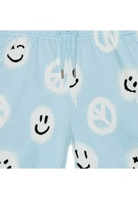 Světle modré šortky s tkaničkou v pase, na kterých se nacházejí černé vzory s úsměvnými obličeji a symbolem míru na bílém kruhovém pozadí.