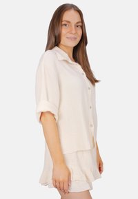 Light beige two-piece outfit featuring a textured button-up shirt with rolled sleeves and a matching ruffled skirt. Cotton material.