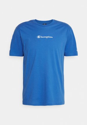 Niebieski t-shirt z krótkim rękawem z białym logo "Champion" na środku klatki piersiowej oraz małym logo na lewym rękawie.