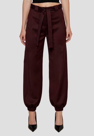Pantaloni larghi color bordeaux realizzati in tessuto morbido, con cintura frontale annodata, polsini elasticizzati e due tasche anteriori. Tacchi alti neri.