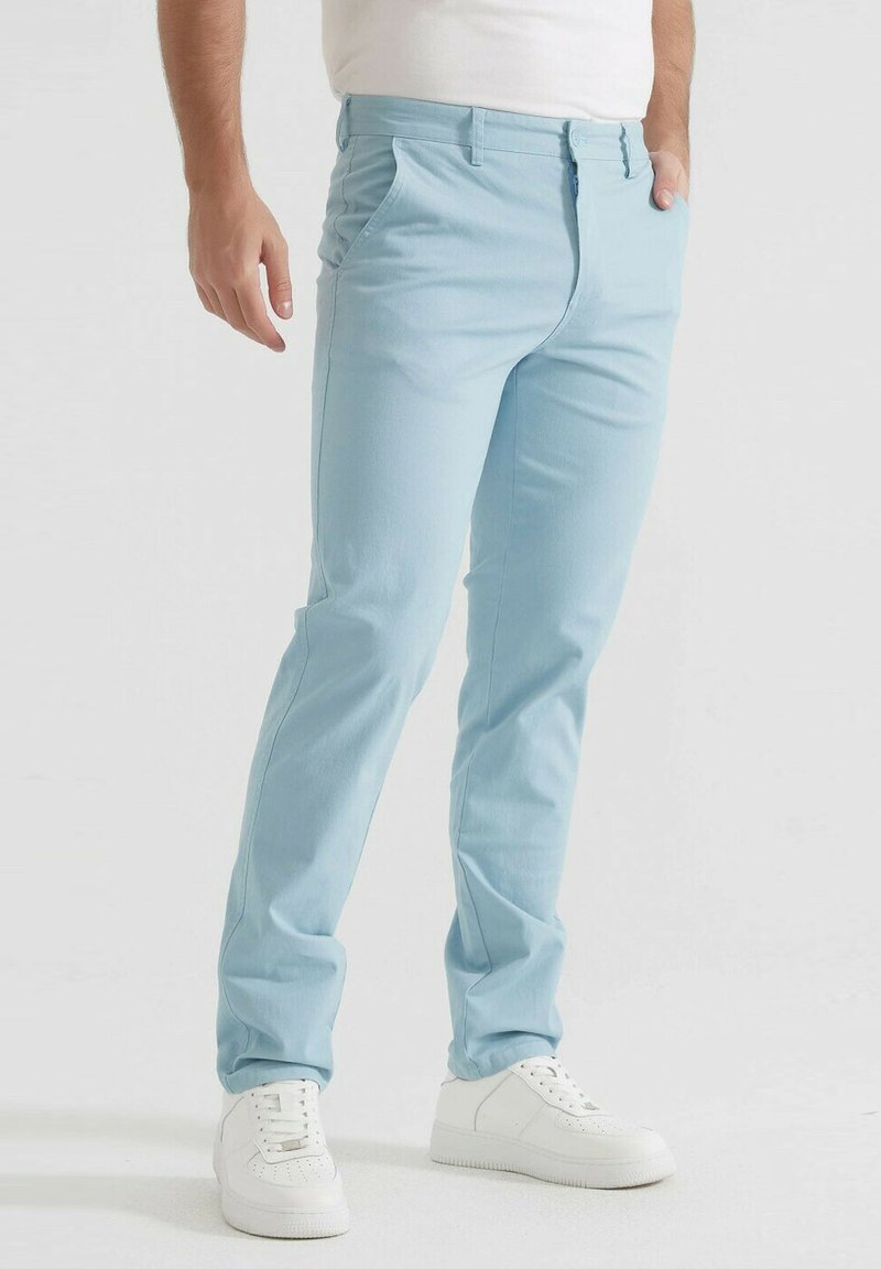 Pantalon bleu clair en tissu doux avec une coupe ajustée. Doté de poches avant et d'une fermeture à bouton à la taille, associé à des baskets blanches.