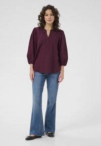 Burgundy blouse with puffed sleeves and V-neck, featuring a subtle pattern. Paired with flared denim jeans and black flats.