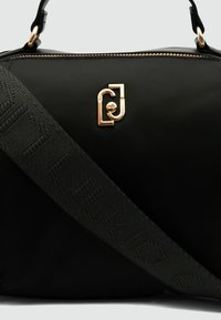 Borsa a mano nera in nylon con logo dorato, dotata di una tracolla nera testurizzata con motivi ripetuti e chiusura a zip.