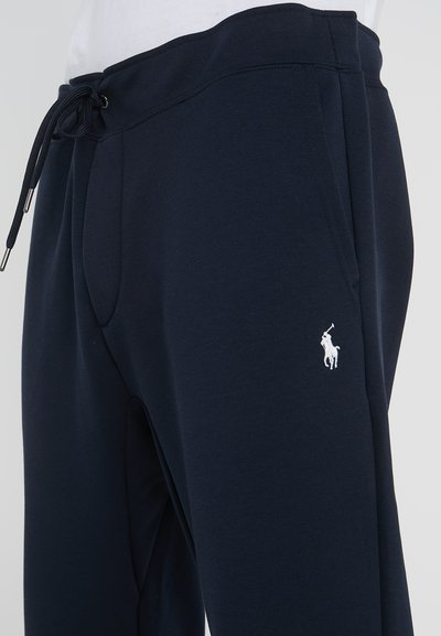 Pantalons de survêtement bleu marine en coton, avec une taille à cordon de serrage, des poches latérales et un petit logo blanc brodé sur la cuisse gauche.