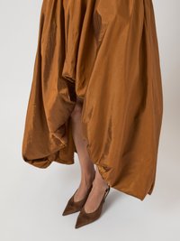 Woman wearing a shiny, voluminous brown skirt paired with pointed-toe brown slingback heels, set against a plain light background.