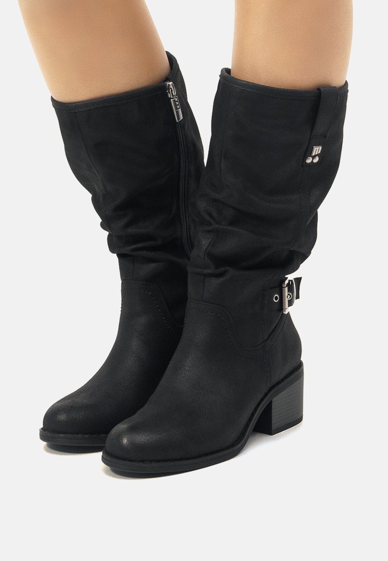 Botas negras de estilo de cuero sintético hasta la rodilla con un diseño holgado, cremallera lateral, acentos en hardware plateado y tacón cuadrado. Acabado texturizado.