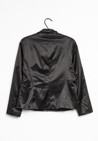 Svart glänsande satinblazer som hänger på en svart galge mot en vit bakgrund, sedd bakifrån.