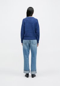 Blauer Strickpulli mit weitem Kragen, kombiniert mit hellblauen Jeans aus Denim mit umgeschlagenem Saum. Sanfte Textur, lässige Passform und entspannte Silhouette.