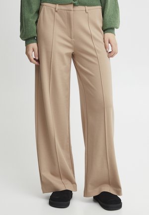 Beige wijde broek met een gladde textuur, voorzien van voorplooien en zijzakken, gecombineerd met zwarte instappers en een groene top.