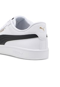 Sapatilha branca com detalhes pretos, parte superior em sintético suave, colarinho acolchoado e detalhe com logótipo no calcanhar. Apresenta uma sola de borracha texturizada.