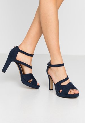 Granatowe zamszowe sandały na wysokim obcasie z krzyżującymi się paskami, odkrytą palcą i platformą dla dodatkowej wysokości.