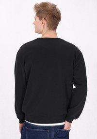Sweatshirt negru cu guler rotund, croială relaxată și manșete din material ribbit. Fabricat dintr-un material moale, având un spate simplu și un design minimalist.