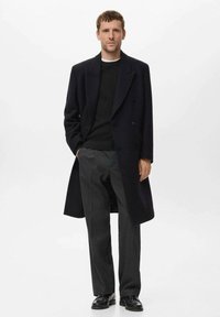 Navy wool overcoat with a double-breasted design, worn over a black knit sweater and gray trousers, paired with black shoes.