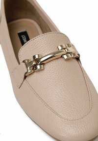 Lichtroze leren loafers met een gestructureerde afwerking en gouden hardwareaccenten aan de voorkant. Rond neussluiting en gestikte details.