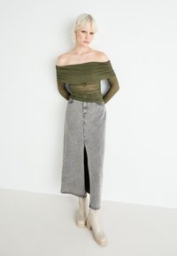 Olivgrüne schulterfreie transparente Bluse, kombiniert mit einem grauen Denim-Maxirock mit einem vorderen Schlitz, ergänzt durch beiges Absatzstiefel.