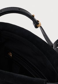Interiér černé semišové kabelky s látkovou podšívkou, kapsou na zip a nastavitelným koženým popruhem s mosaznou sponou.