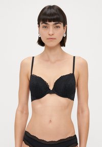 Soutien-gorge push-up en dentelle noire avec des bords festonnés et des bretelles réglables, présentant un motif floral et une texture lisse.