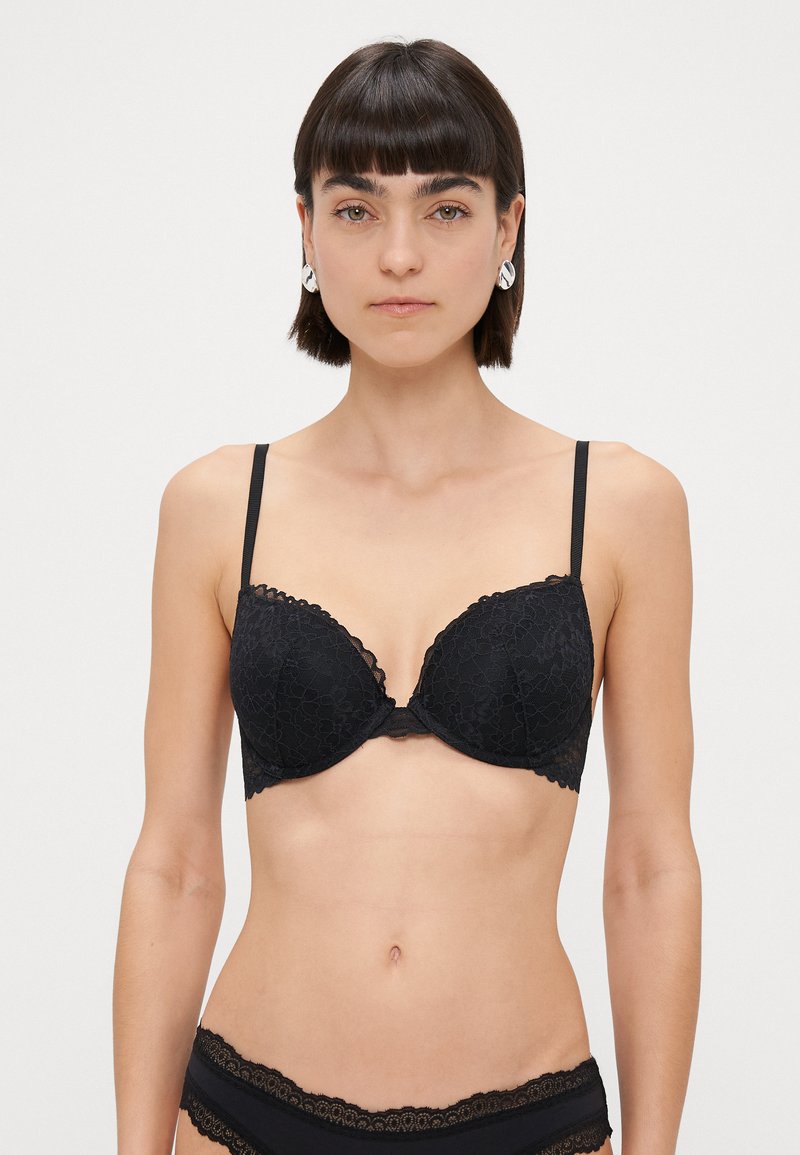 Soutien-gorge push-up en dentelle noire avec des bords festonnés et des bretelles réglables, présentant un motif floral et une texture lisse.