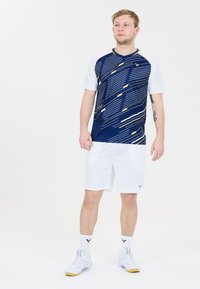Herrers sportklädsel bestående av en mönstrad kortärmad skjorta i marinblått med vita ärmar, tillsammans med vita shorts och vita skor.