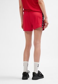 Rode atletische shorts met zwarte chevron-patroonaccenten, gecombineerd met zwarte sportschoenen en witte sokken met een chevron-ontwerp.