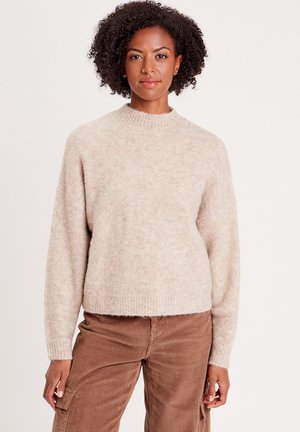 Pull en tricot beige avec un col monté, des manches longues et un ourlet côtelé. Le tissu a une texture douce et pelucheuse avec des variations de motifs subtiles.