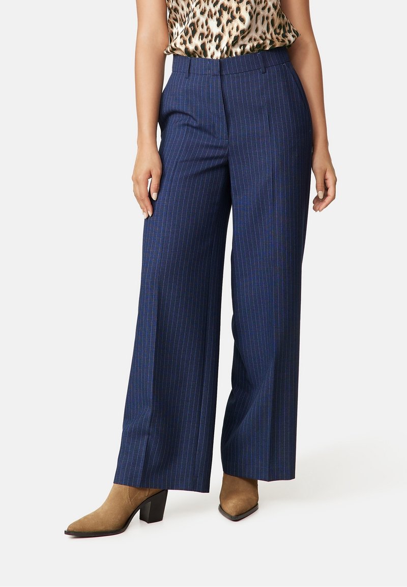 Marinblå vida byxor med vertikala vita och blå ränder, tillverkade av ett slätt tyg. Har en midjehöjd som är medelhög och framfickor.