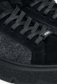 Baskets noires avec une tige en daim et un panneau en laine grise texturée, semelle en caoutchouc épaisse et lacets noirs plats. Étiquette de logo incluse.