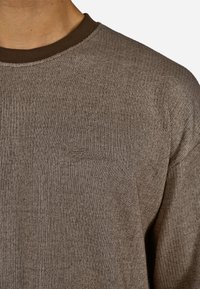 Barna bordás pulóver kerek nyakkivágással és sötétbarna gallérral. Diszkrét varrási részlet a márka logójával a mellkason.