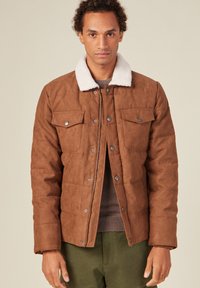 Brun vadderad jacka med krage av syntetisk shearling, tryckknappar och två bröstfickor. Texturerad tyg med en slät yta.