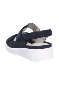 Sandale en daim bleu marine avec une sangle à crochets et boucle, talon ouvert et épaisse semelle blanche. Présente un design découpé pour la respirabilité et le confort.