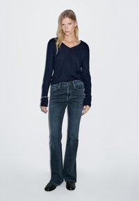 Námořnická dlouhá ruka V-čelní top spojený s tmavě modrými zvonovými džíny. Hladká textura, volný design, přiléhavý pas a jemné švy.