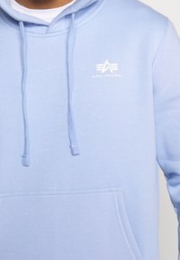 Felpa azzurra chiara in misto cotone con tasca a marsupio, cappuccio con cordino e dettaglio logo bianco sul petto. Tessuto morbido.