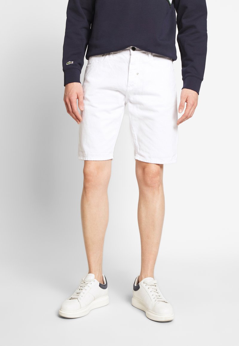 Shorts bianchi in cotone con taglio dritto, dotati di tasche frontali e zip con bottone. Abbinati a sneakers bianche con dettagli blu navy.