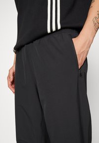 Czarne spodnie sportowe wykonane z lekkiego materiału, z elastycznym paskiem w talii, bocznymi kieszeniami i gładką teksturą.