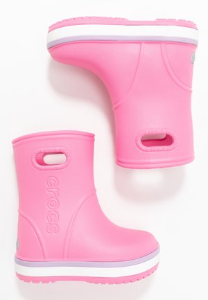 Pár jasně růžových Crocs holínek do poloviny lýtek s bílými a levandulově pruhovanými podrážkami a vestavěnými otvory pro ruce blízko horní části.