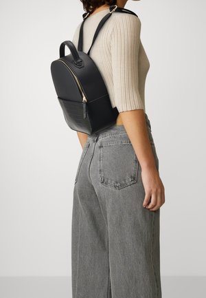 Black leather backpack with a rounded shape, gold zipper, and a textured embossed panel at the bottom. Adjustable straps and a top handle.