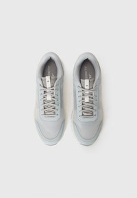 Sapatilhas cinza-claro com um acabamento texturizado, atacadores planos e uma faixa branca de destaque. Ponta arredondada e sola amortecida para conforto.