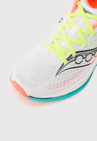 Zapatilla de running blanca de malla con cordones en amarillo neón, un logo negro y acentos en turquesa y coral en la suela y el borde superior.