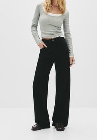 Jean noir à jambes larges avec une taille haute, doté de deux poches avant et d'une fermeture à bouton. Associé à un haut gris à manches longues.