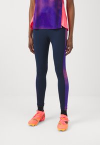Leggings azul-marinho com detalhes em gradiente roxo e rosa, combinados com chuteiras de futebol rosa brilhante apresentando um design texturizado e detalhes de atacadores.