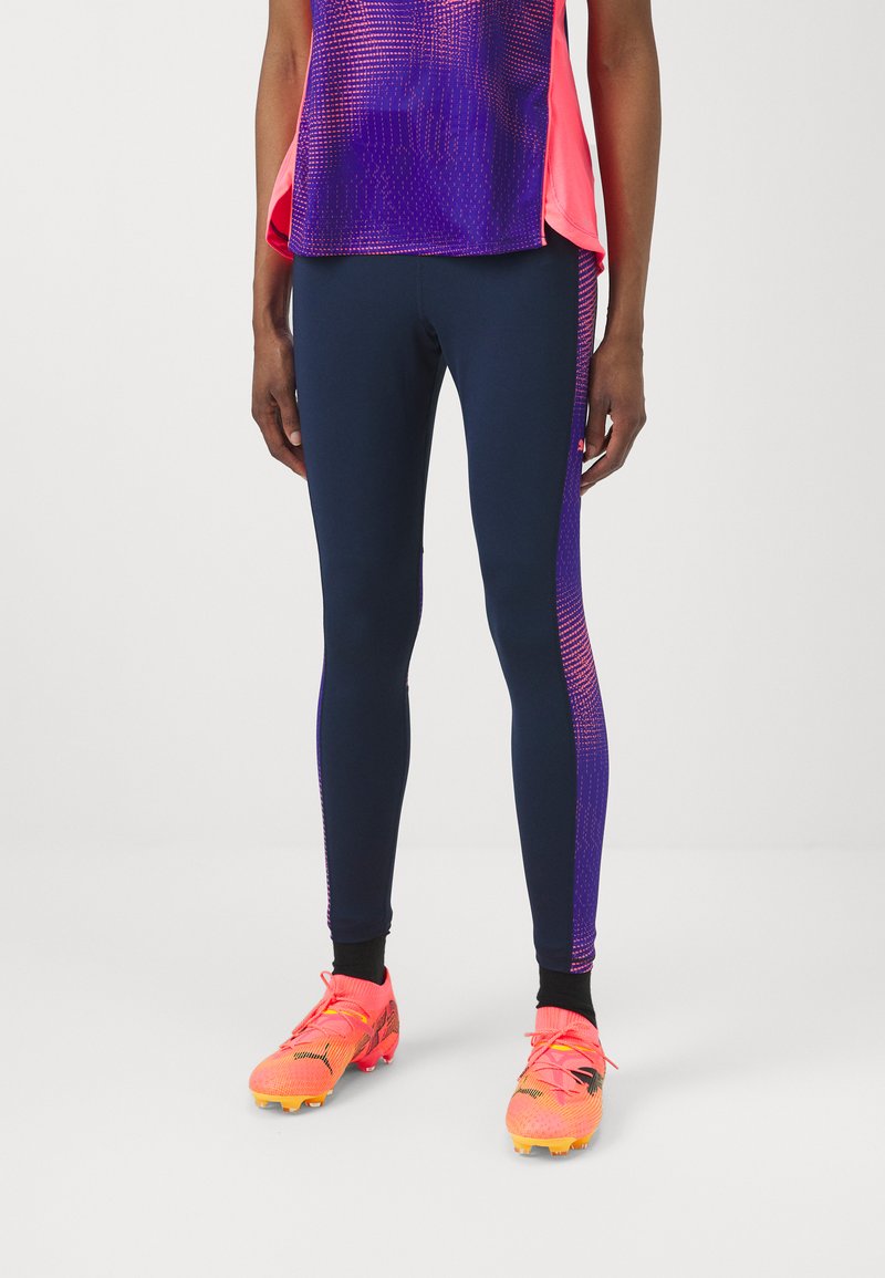 Leggings blu con accenti in gradiente viola e rosa, abbinati a scarpe da calcio rosa brillante con un design testurizzato e dettagli di lacci.
