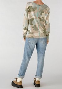 Maglia a maniche lunghe in un motivo camouflage tenue con tonalità di beige, verde e blu. Presenta un taglio dritto e un dettaglio di cucitura turchese. Abbinata a jeans azzurri chiari.