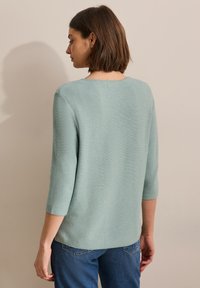 Maglia a maglia verde chiaro con maniche tre quarti, scollatura rotonda e una texture morbida, abbinata a jeans di denim blu.